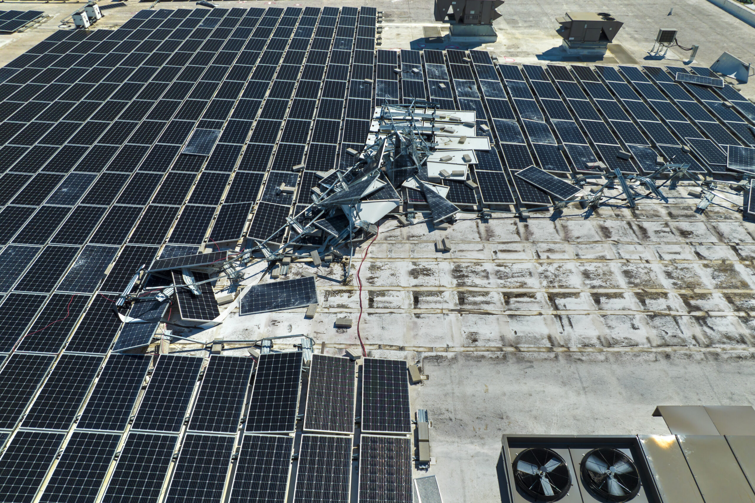 Destroyed by hurricane winds broken down photovoltaic solar panels mounted on industrial building roof for producing green ecological electricity. Consequences of natural disaster in Florida.